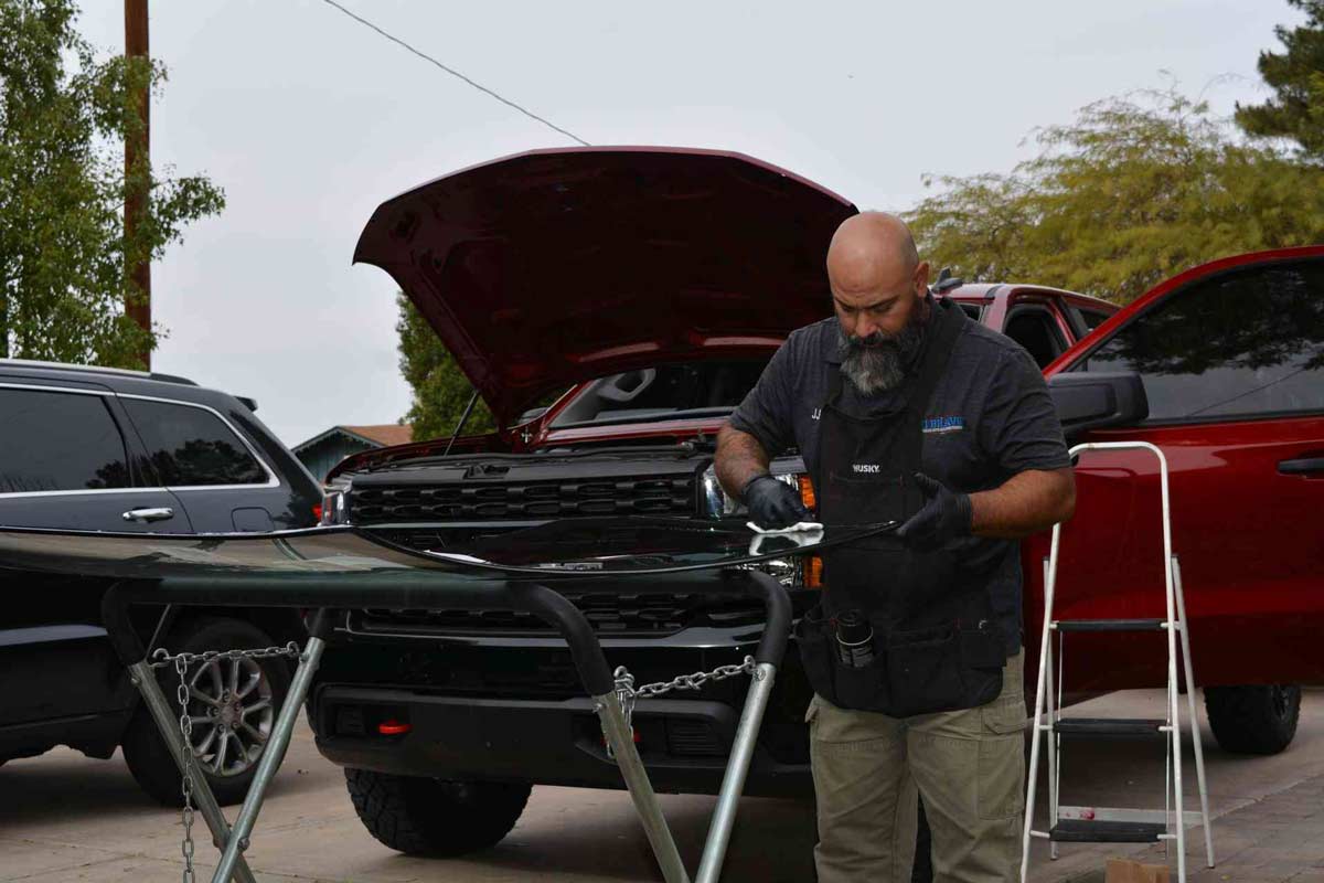 A man is seen fixing the windshield of a red car in Peoria, AZ