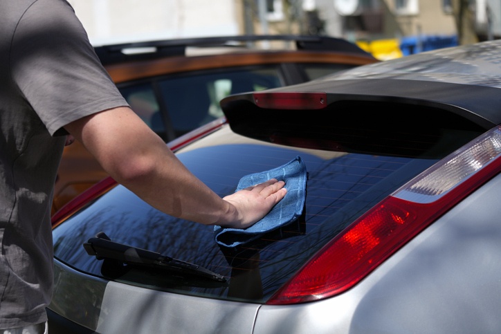 A man is cleaning the rear window of a car in Peoria and Surprise