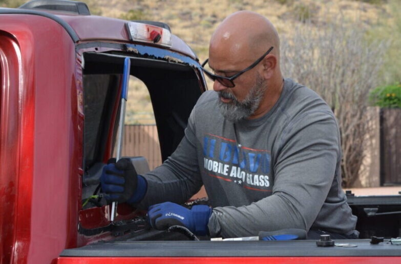 Auto glass technician removing rear window from truck outdoors in Surprise, AZ