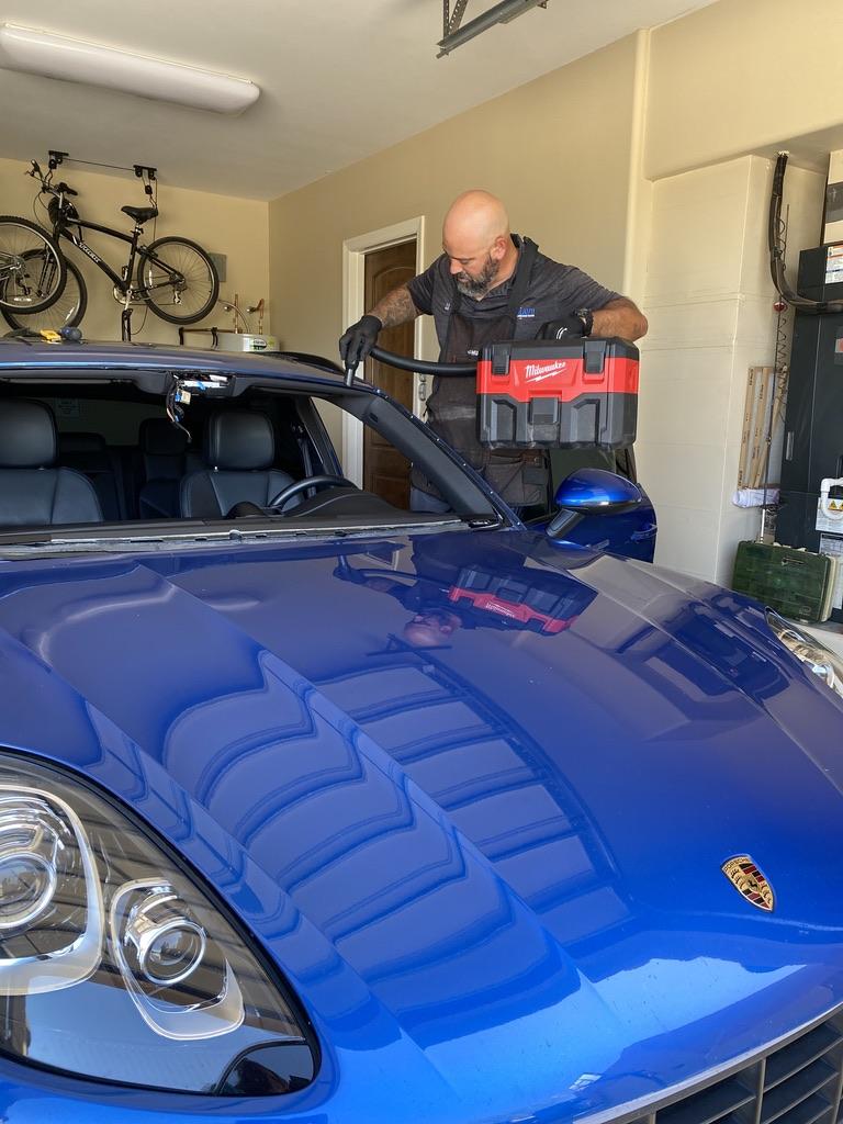 Auto glass technician installing windshield on blue car inside home garage in Surprise, AZ